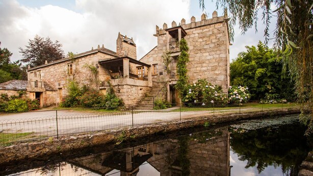 Un edificio de piedra con una torre, un pequeño puente sobre el agua y una valla.