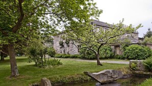 Un edificio de piedra con un jardín, un estanque y un gran árbol en primer plano.