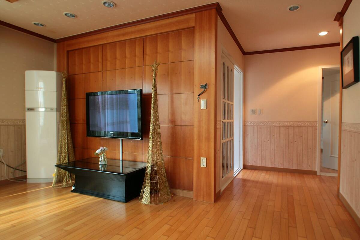 A hotel room with wooden paneling, a flat-screen TV, a black console table, and a decorative golden tree.