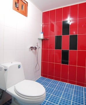 Un baño con inodoro blanco, ducha con cabina de vidrio y paredes con azulejos rojos y negros.