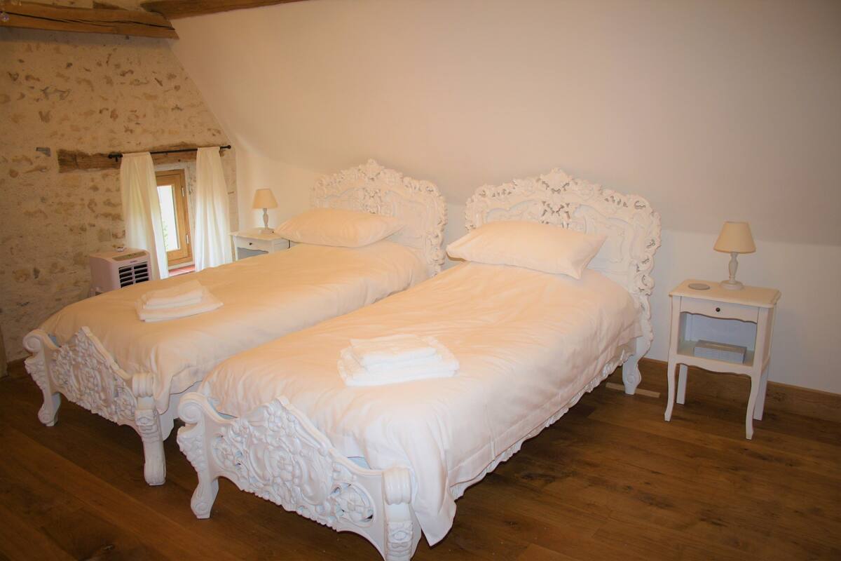 A double bed with ornate headboard and footboard, two bedside tables with lamps, and a stone wall.