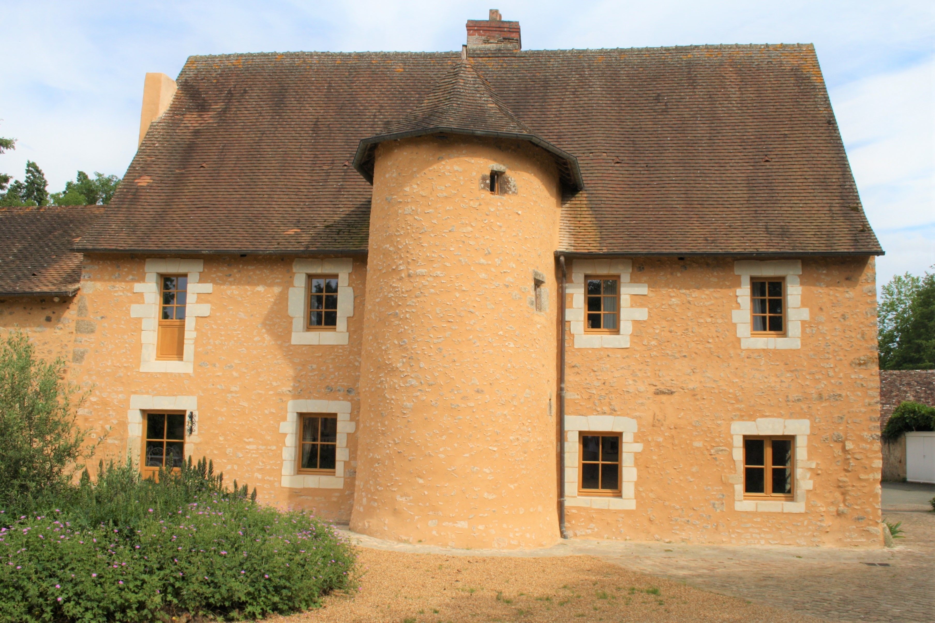 Un bâtiment en pierre doté d’une tour arrondie, de nombreuses fenêtres et d’un toit en pente.