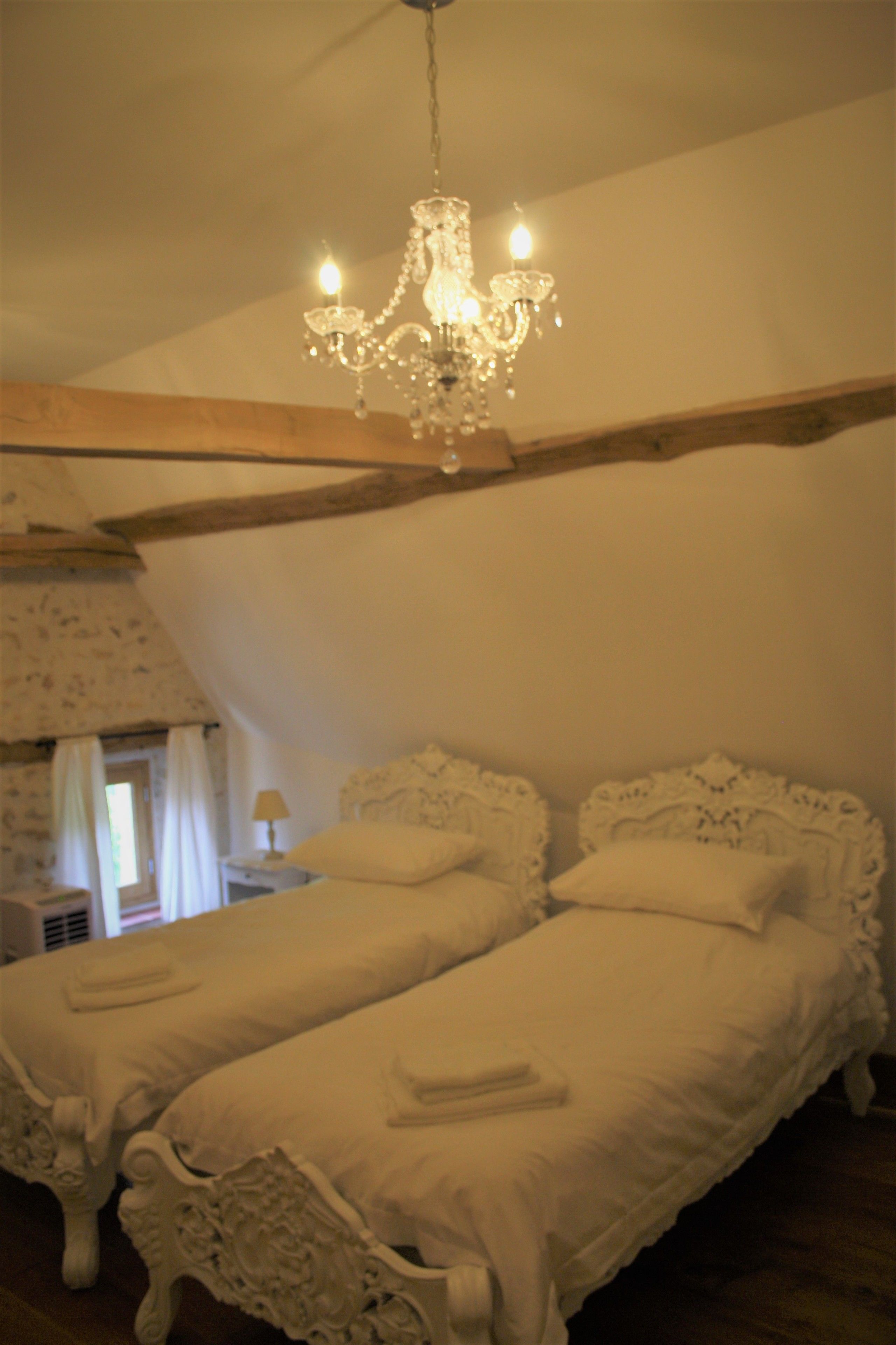 A bedroom with two beds, a chandelier, and a nightstand with a lamp.