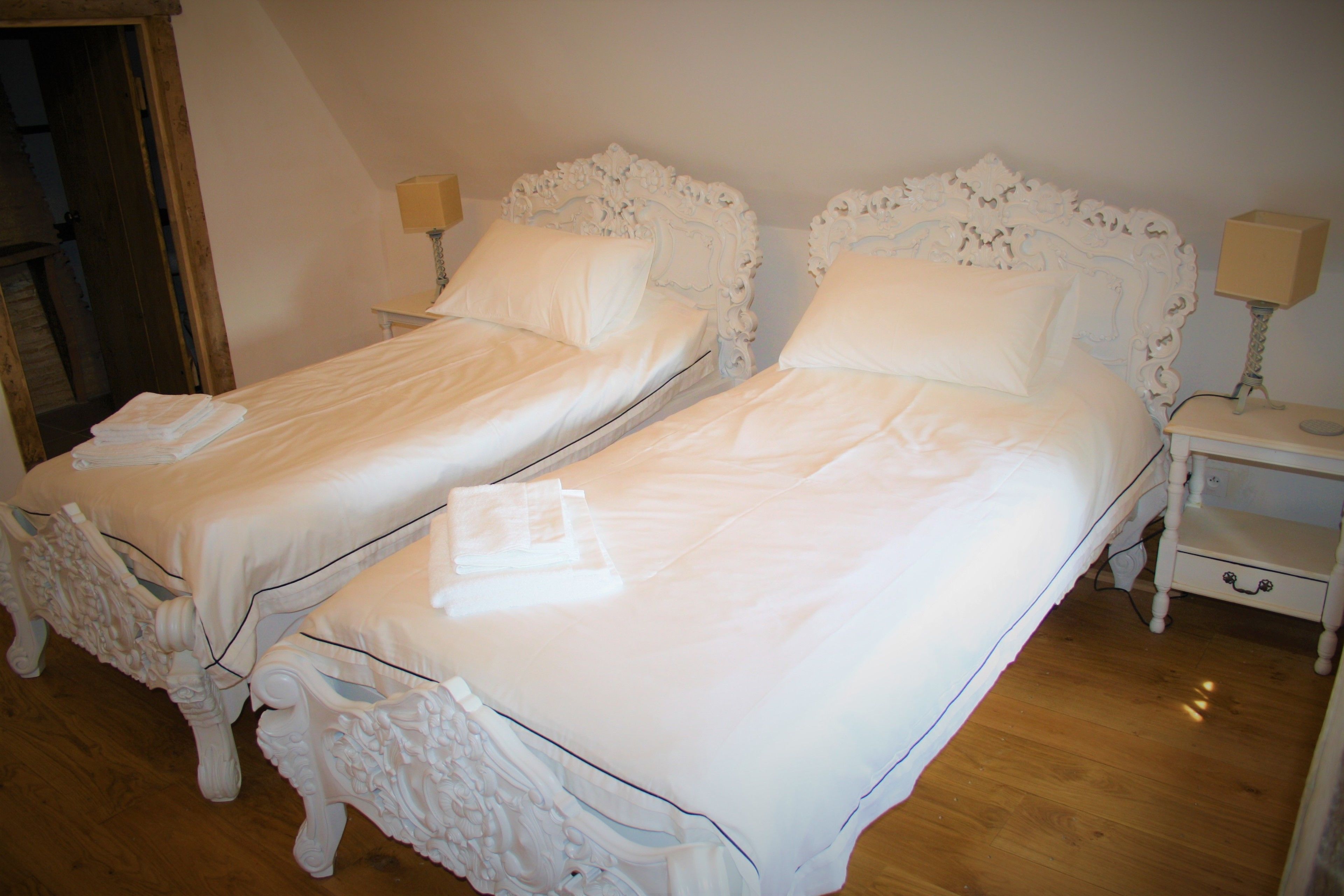 Dos camas blancas con cabeceras decoradas en una habitación con suelo de madera.