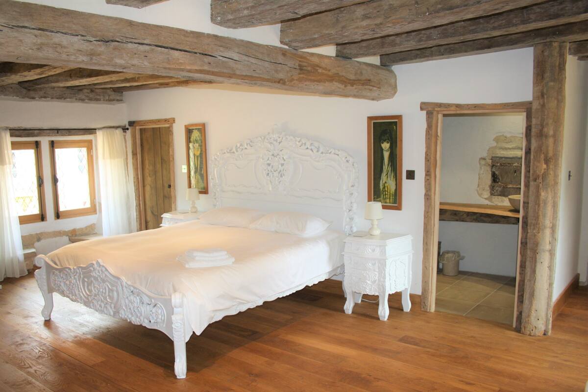 A spacious bedroom with a large bed, wooden beams, and a wooden floor.