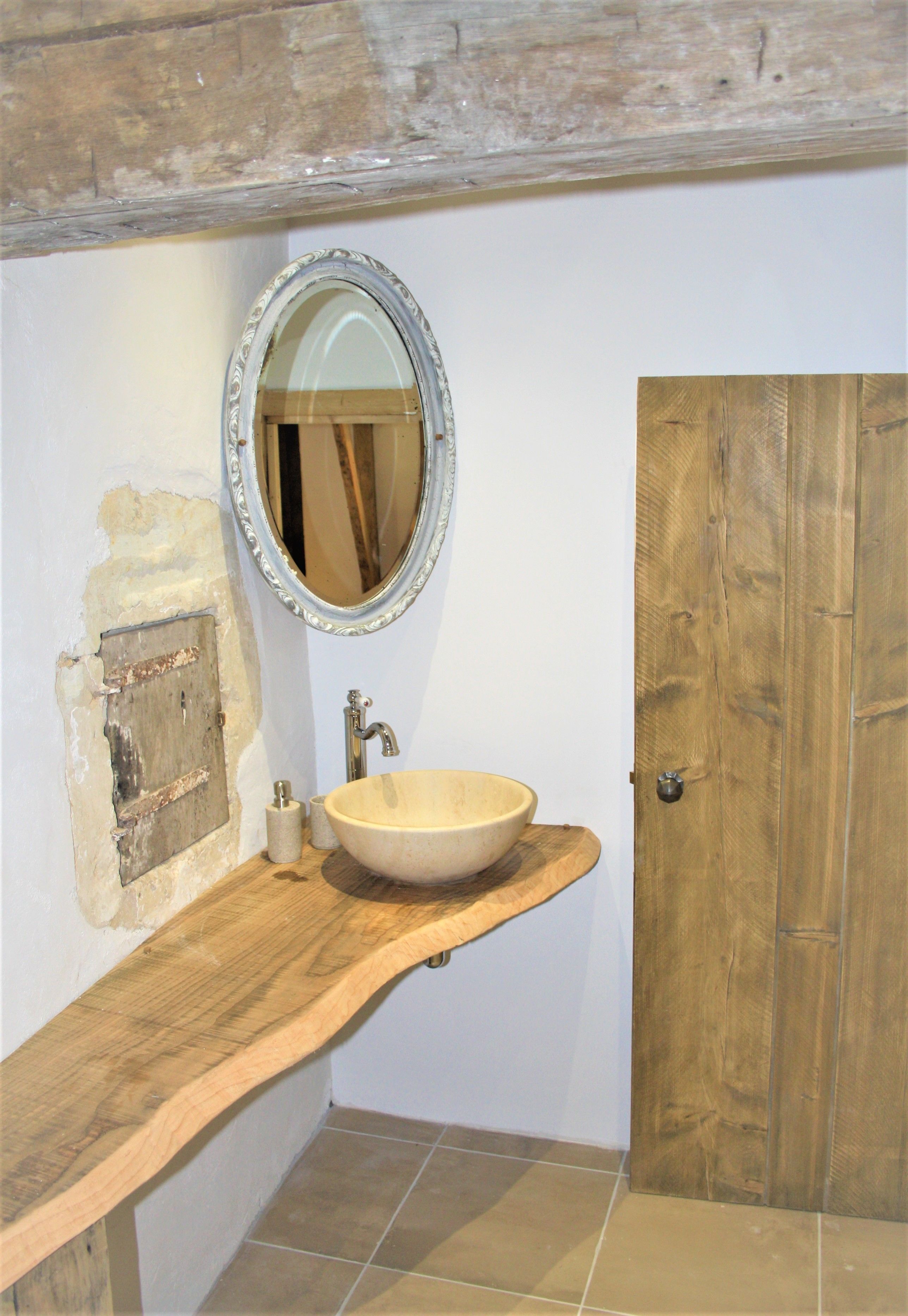 Un baño con tocador de madera, un espejo redondo, un lavabo blanco y una puerta de madera.