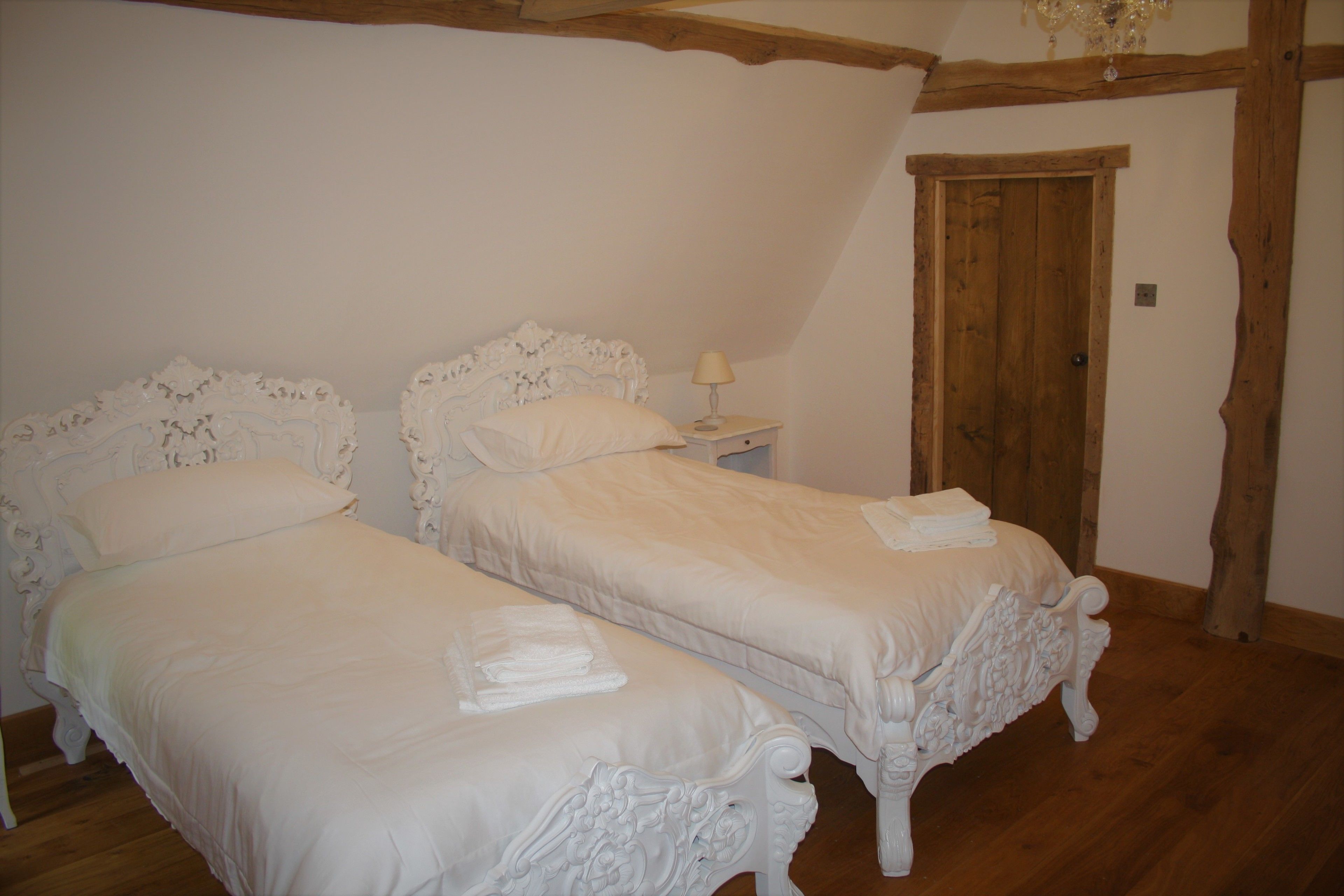 Een slaapkamer met twee bedden, houten balken in het plafond, een houten deur en een nachtkastje met een lamp.