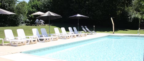 Una piscina al aire libre, sombrillas, sillones reclinables de piscina