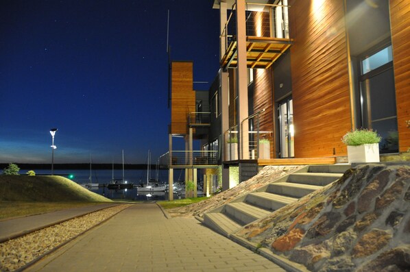 A modern building with a stone staircase leading to a wooden deck overlooking a marina at night.