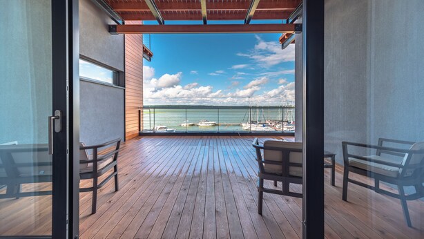 Un balcón con piso de madera, dos sillas y vista al mar y a los barcos.