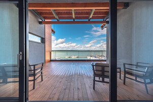 Un balcón con piso de madera, dos sillas y vista al mar y a los barcos.