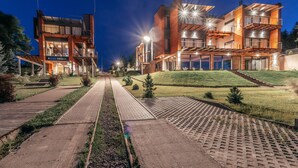 Un hotel moderno de varios pisos con un patio central, asientos al aire libre y una fachada bien iluminada.