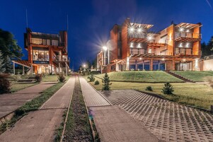 Un hotel moderno de varios pisos con un patio central, asientos al aire libre y una fachada bien iluminada.