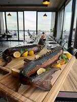 Un plato de mariscos con rodajas de limón sobre una mesa de madera en un restaurante con vista al mar.
