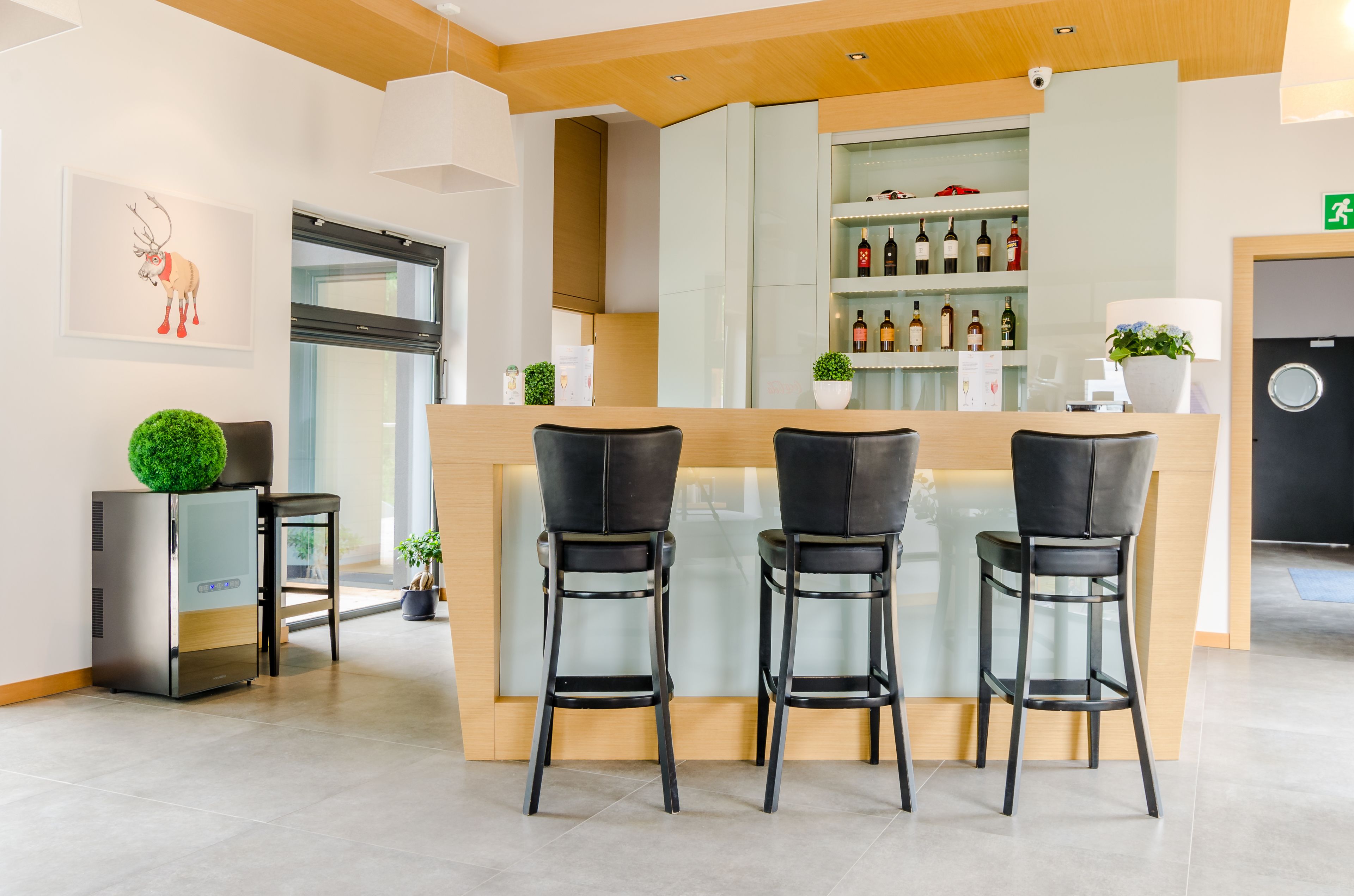 Un área de bar moderna con dos taburetes negros, una barra de madera y una exhibición de vinos.