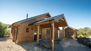A wooden cabin with a sloped roof, a covered porch, and a gravel driveway. - Húsafell Holiday Homes (Borgarbyggd)