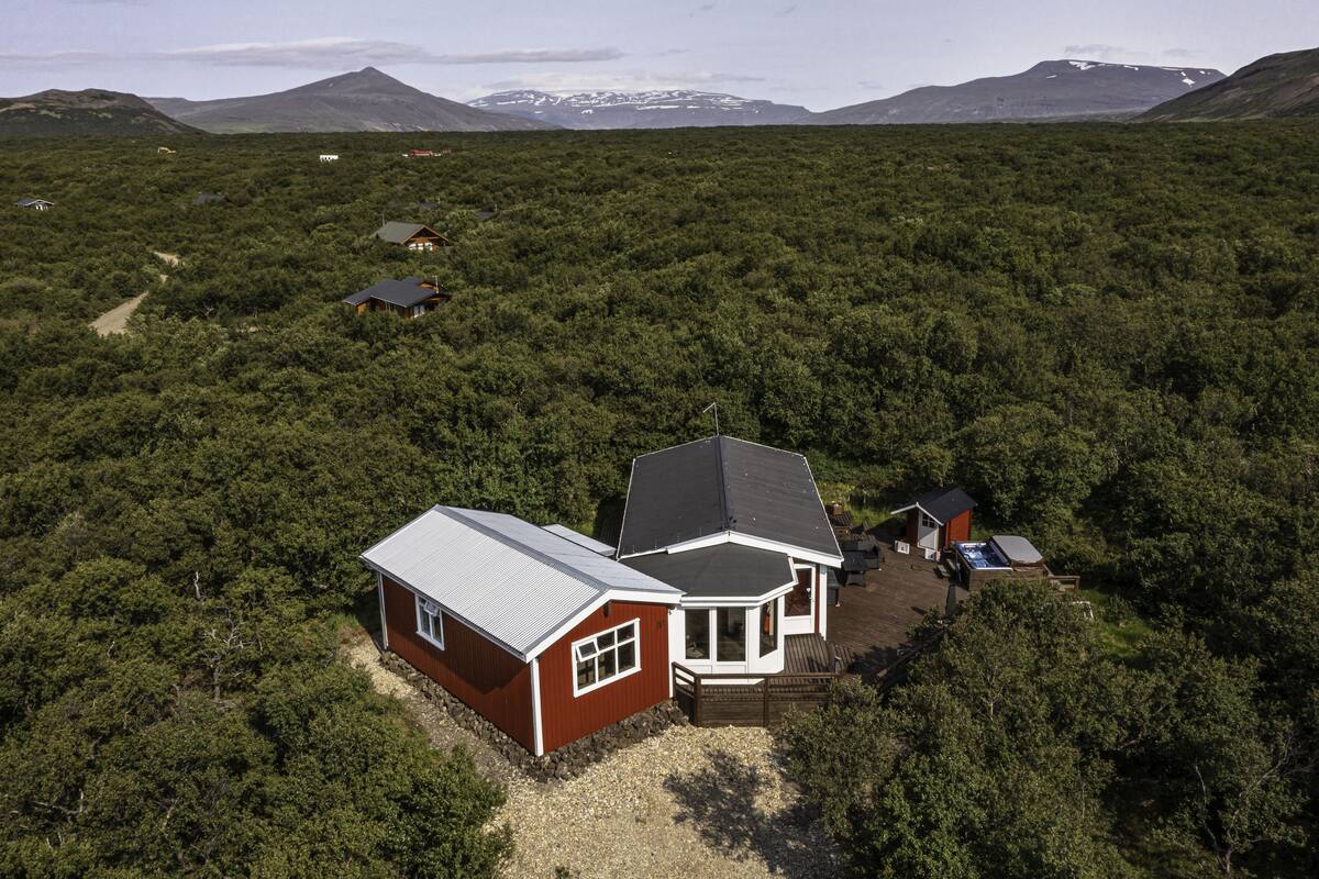 Ein abgelegenes Ferienhaus mit großer Terrasse und Whirlpool, umgeben von dichtem Wald und Bergen im Hintergrund.