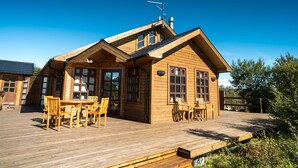 A wooden cabin with a deck, large windows, and a chimney. - Húsafell Holiday Homes (Borgarbyggd)