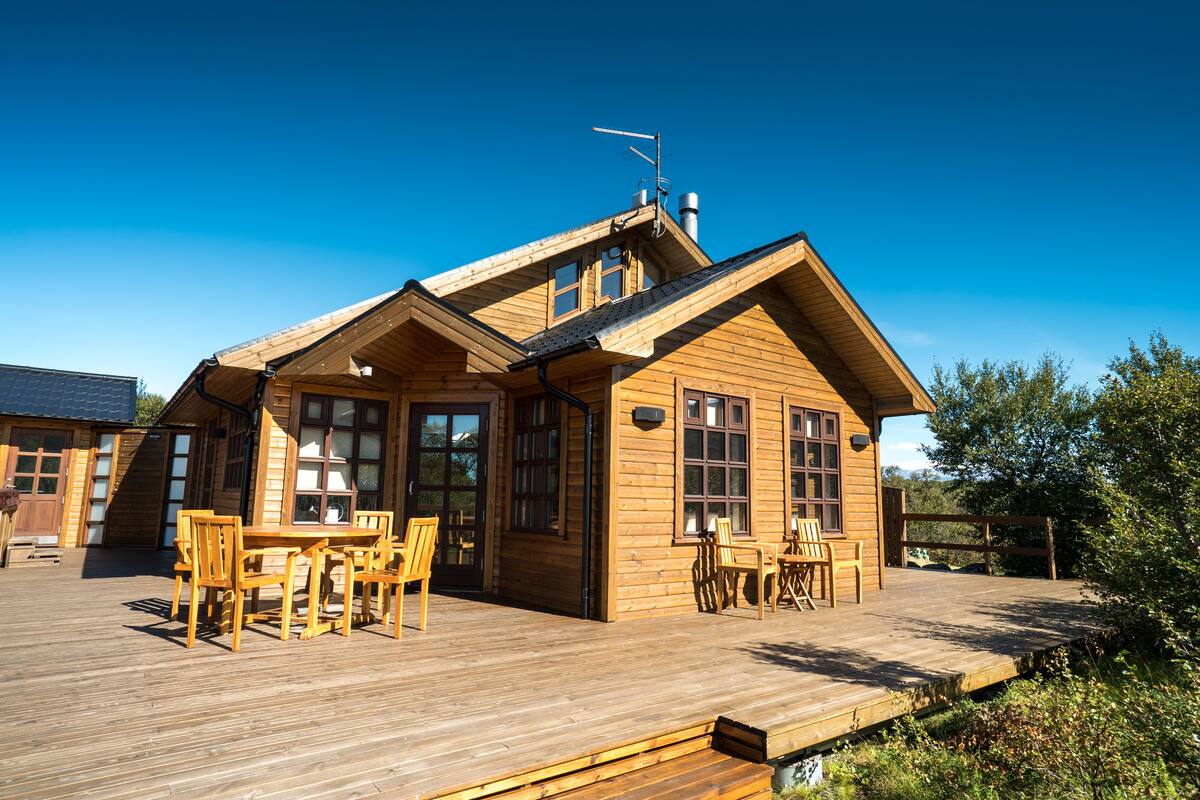 Eine Holzhütte mit Terrasse, großen Fenstern und Schornstein.