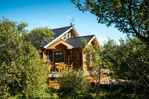 A wooden cabin with a sloped roof, a chimney, and a small porch with chairs.