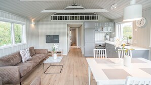 A spacious living area with a sofa, coffee table, and dining table. A kitchen with cabinets and a sink is visible in the background. - Húsafell Holiday Homes (Borgarbyggd)