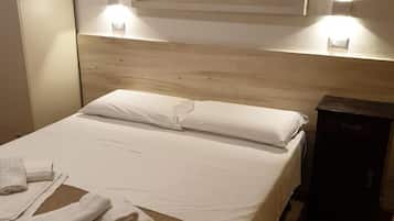 Ein Hotelzimmer mit einem Bett, weißen Leinen, einer gesteppten Bettdecke, einer Wanddekoration mit Fischen, zwei Nachttischlampen und einem kleinen Nachttisch mit einem dunkel gefärbten elektronischen Gerät.