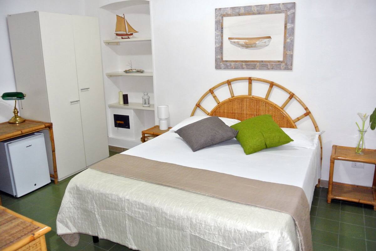 Ein ordentlich eingerichtetes Schlafzimmer mit Bett, Nachttischen, einem Kleiderschrank und einem kleinen Schreibtisch mit Lampe.