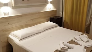 A neatly made bed with white linens, a wooden headboard, a wall-mounted fish decoration, and a yellow curtain. - B&B Kalimaka (San Giovanni a Piro)