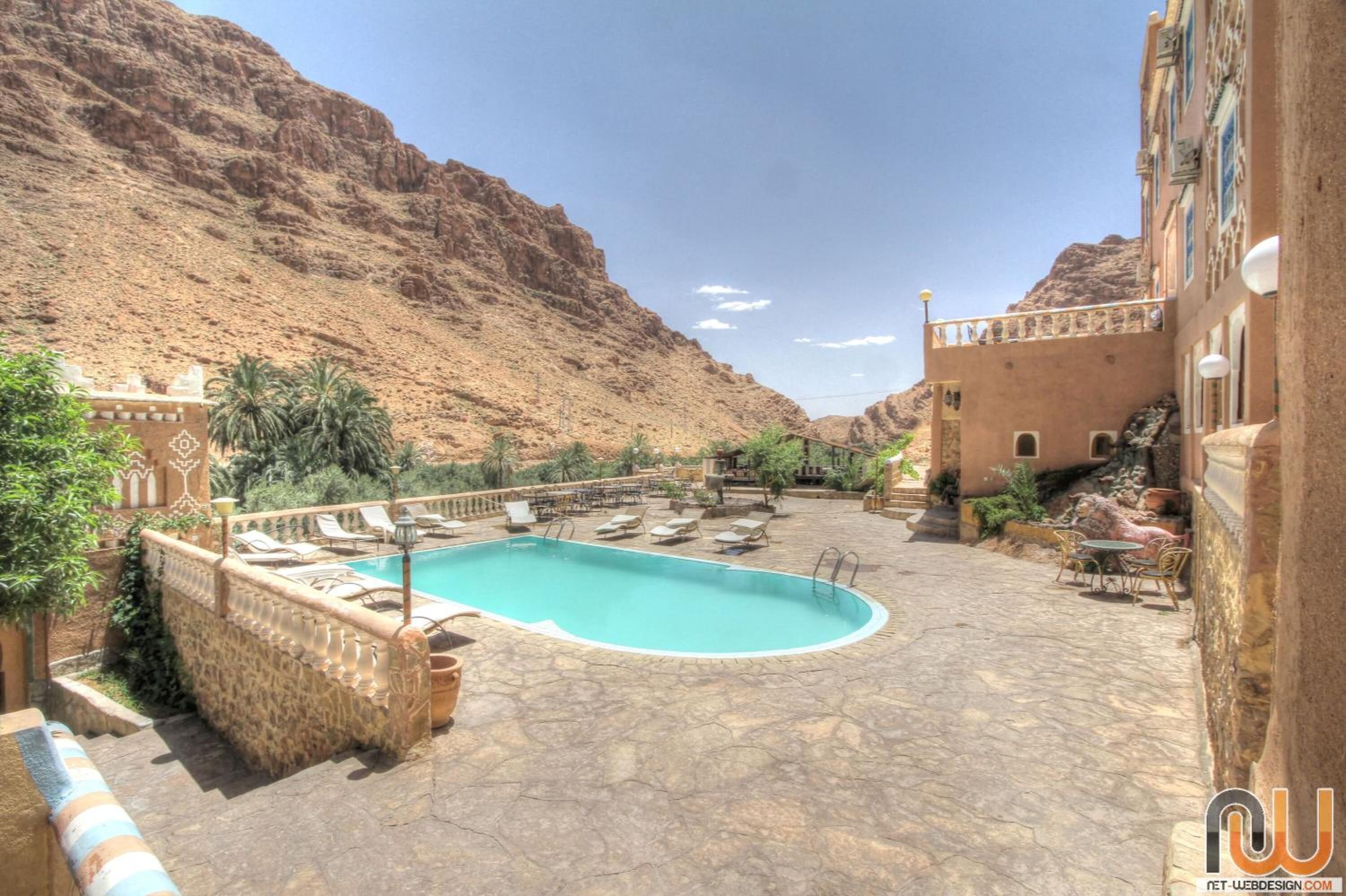 A pool area with lounge chairs and a stone patio, surrounded by desert hills.