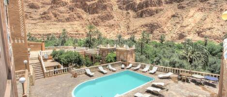 A swimming pool surrounded by lounge chairs and a mountainous backdrop.