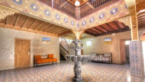 Un interior espacioso con una fuente central, techo ornamentado y baldosas de suelo con diseños.
