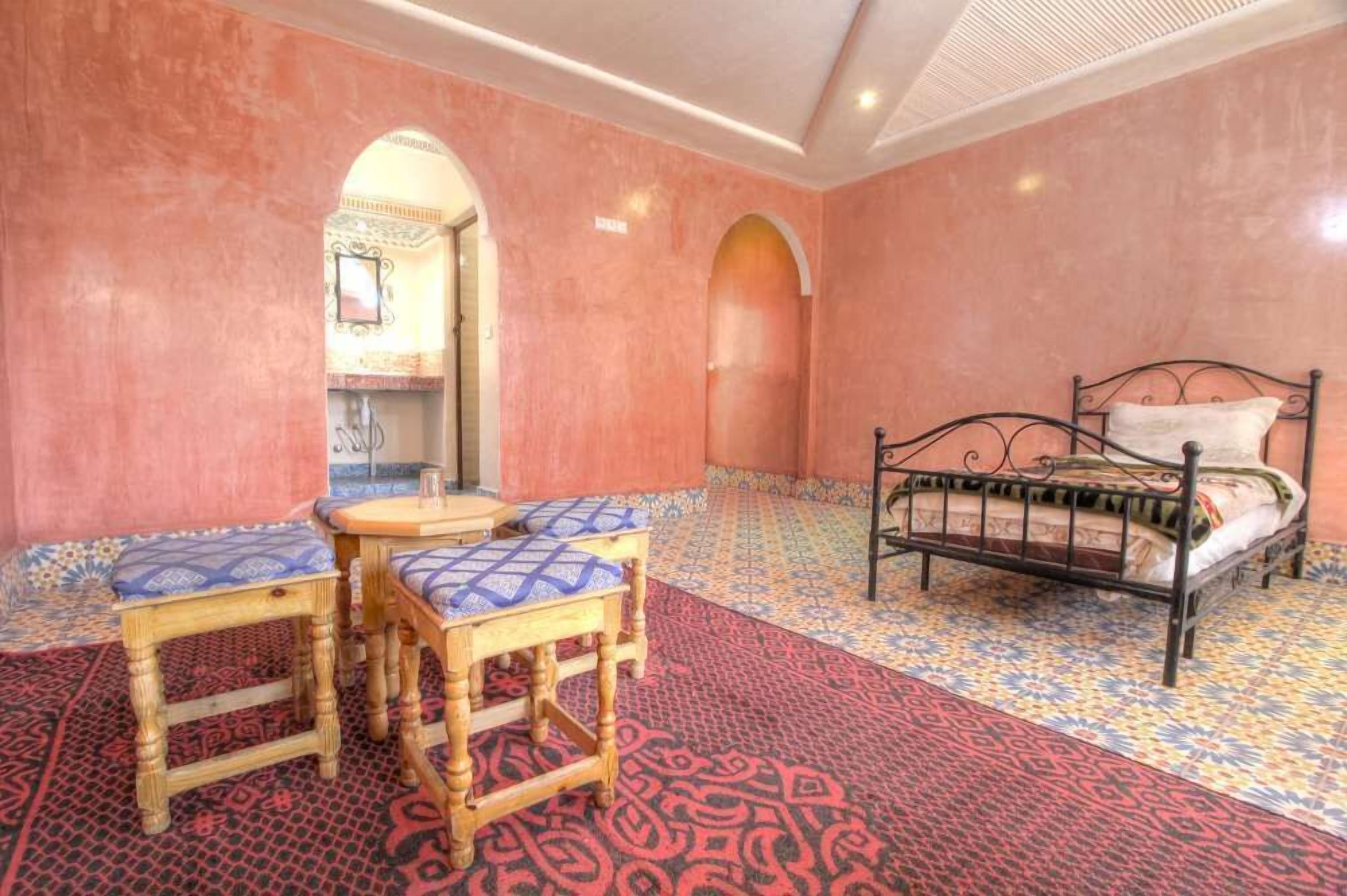 Ein Zimmer mit einem Bett, zwei Holztischen und Teppichen mit Muster.