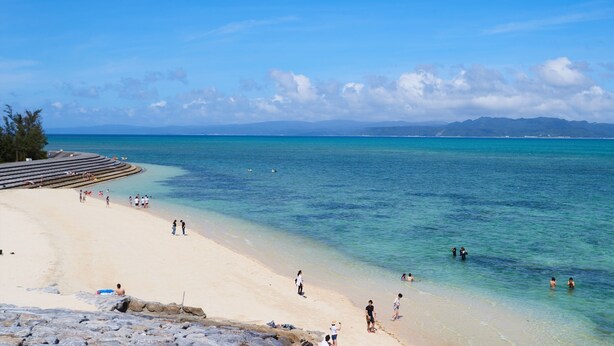 A beach with clear turquoise water, a sandy shore, and a few people enjoying the water.