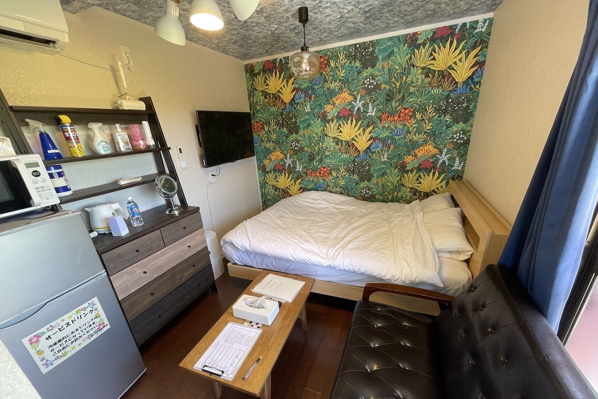 Une chambre d’hôtel de taille réduite, comprenant un lit, une petite table, un canapé, un téléviseur et un mur orné d’une fresque florale.