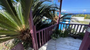 A wooden deck with a railing, surrounded by lush greenery and a clear blue sky.