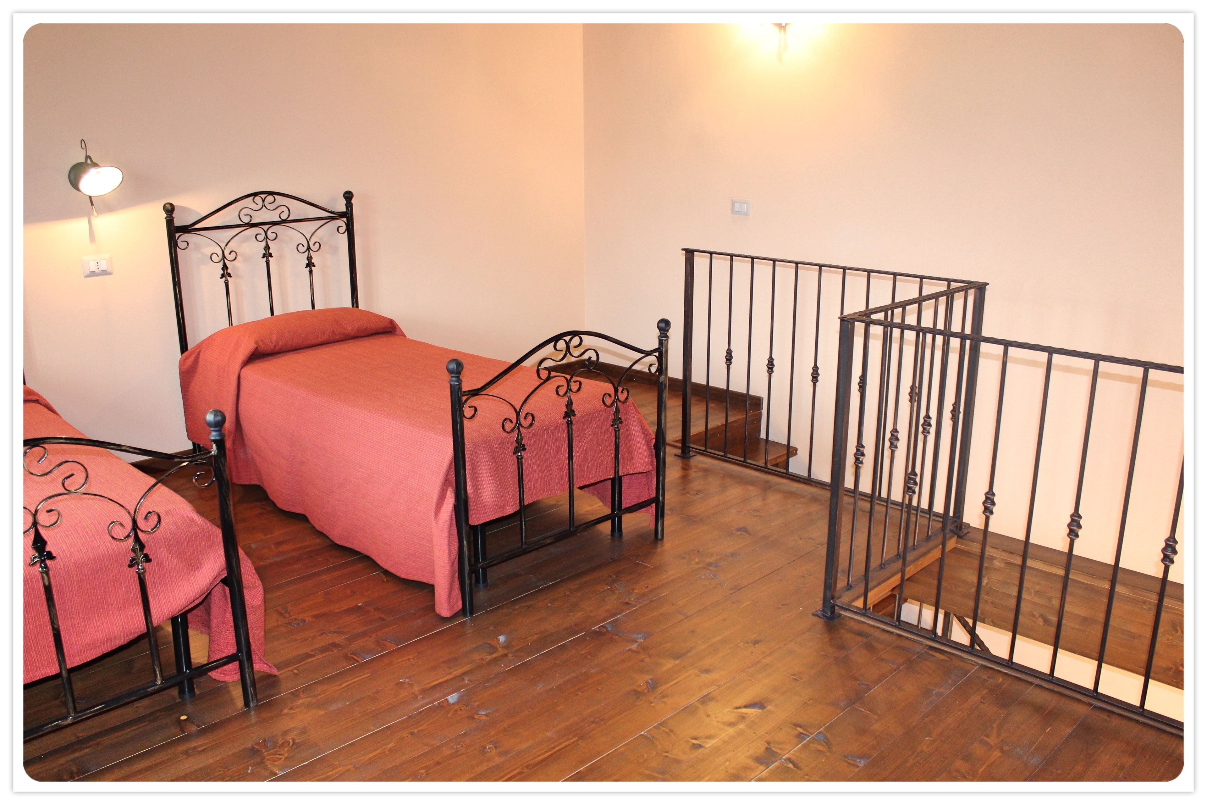 Een slaapkamer met twee bedden, houten vloer, een metalen leuning en een wandlamp.