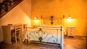 A bedroom with a bed, two bedside tables, a nightstand, a wooden chair, and a staircase. - Agriturismo Aurea (Crucoli)