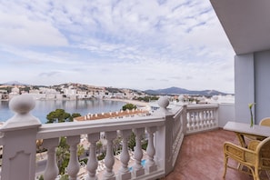 Un balcón con vistas a un pueblo costero, una piscina y montañas al fondo.