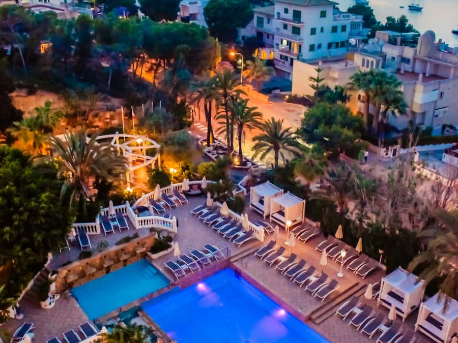A resort with a swimming pool, lounge chairs, and a view of the sea at sunset.