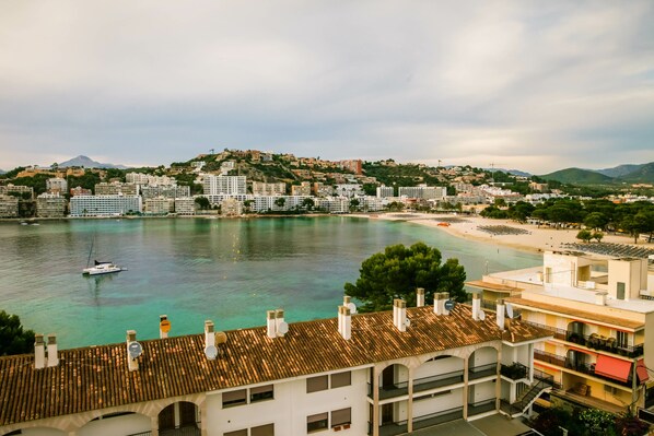 A coastal cityscape with buildings, a beach, and a boat on the water. - Bahia del Sol (Calvia)