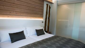 Un dormitorio con cama, ropa de cama blanca, cabecera de madera y mesita de noche con lámpara.