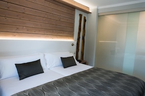 Un dormitorio con cama, ropa de cama blanca, cabecera de madera y mesita de noche con lámpara.