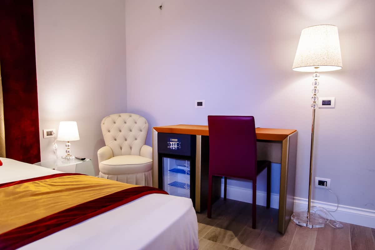 A hotel room with a bed, a desk, a chair, a lamp, and a minibar.