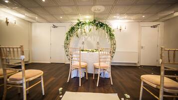 A wedding ceremony setup with a white table, two chairs, and a floral arch.