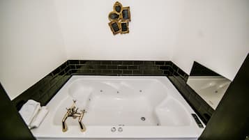 Una vasca da bagno bianca con dettagli dorati, pareti rivestite in piastrelle nere e una piccola targa decorativa sopra.