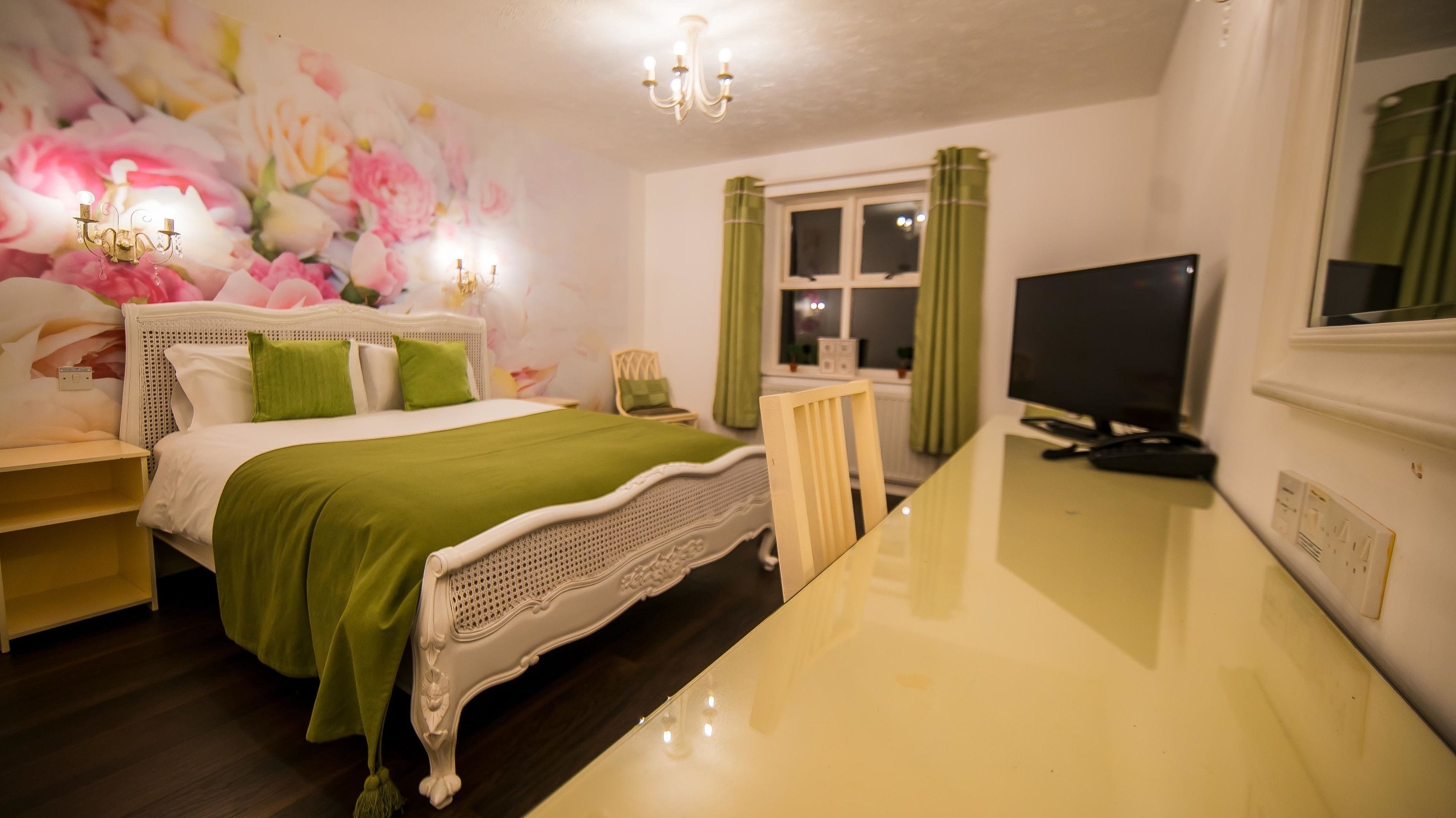A bedroom with a bed, a desk, a television, and a wall with floral wallpaper.