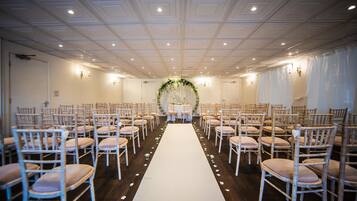 A wedding ceremony setup with rows of chairs, a white aisle, and a floral arch.