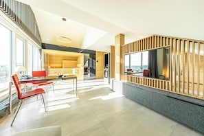 A modern interior with a dining area, kitchen, and a large window offering a view. - FAIR RESORT All Inclusive Wellness & SPA Hotel Jena (Zollnitz)