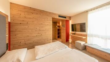 A modern hotel room with a wooden wall, a bed with white linens, a small seating area, and a TV mounted on the wall.