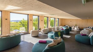 A spacious room with large windows, multiple seating areas, and a view of greenery outside. - FAIR RESORT All Inclusive Wellness & SPA Hotel Jena (Zollnitz)